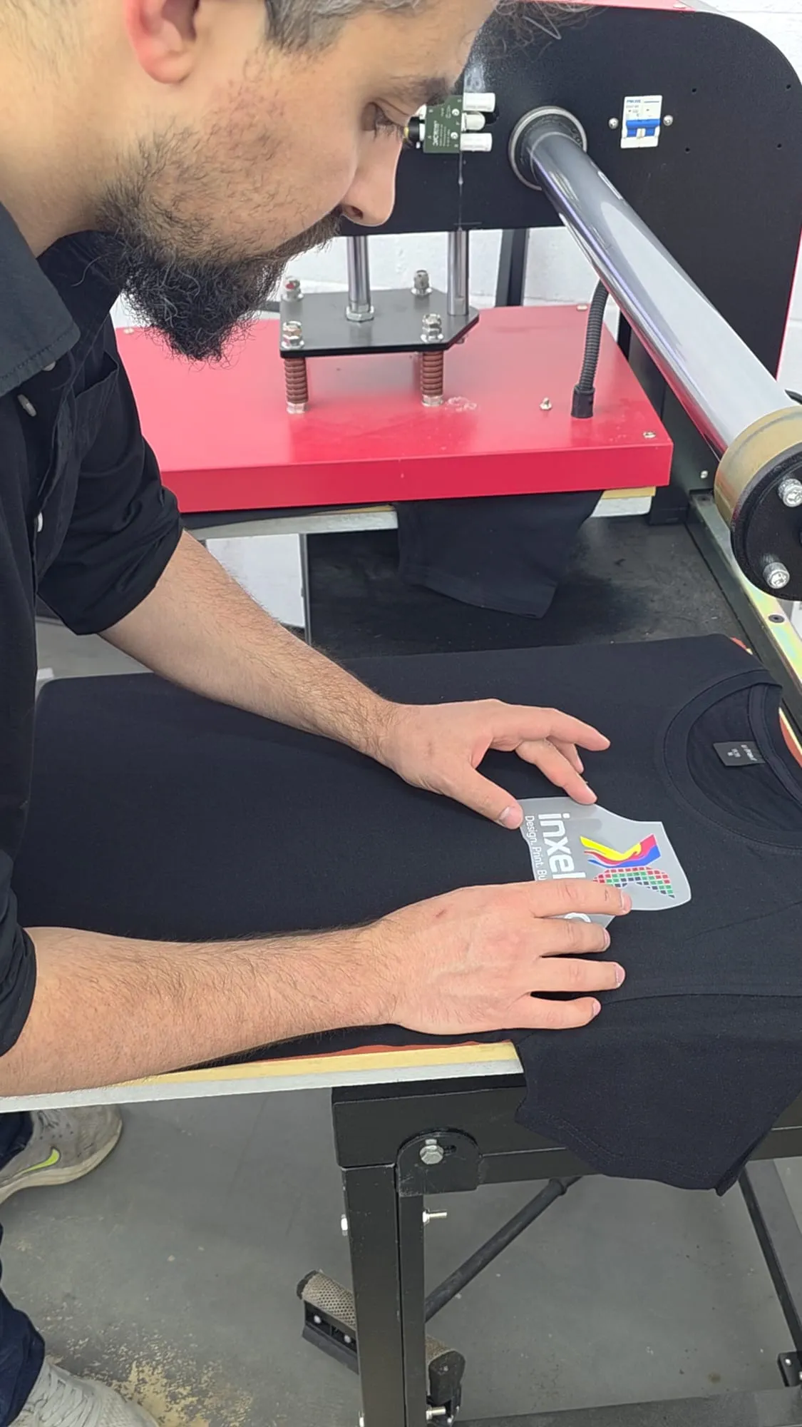A person leans over a heat press and lines up a printed transfer on a black T-shirt with both hands.