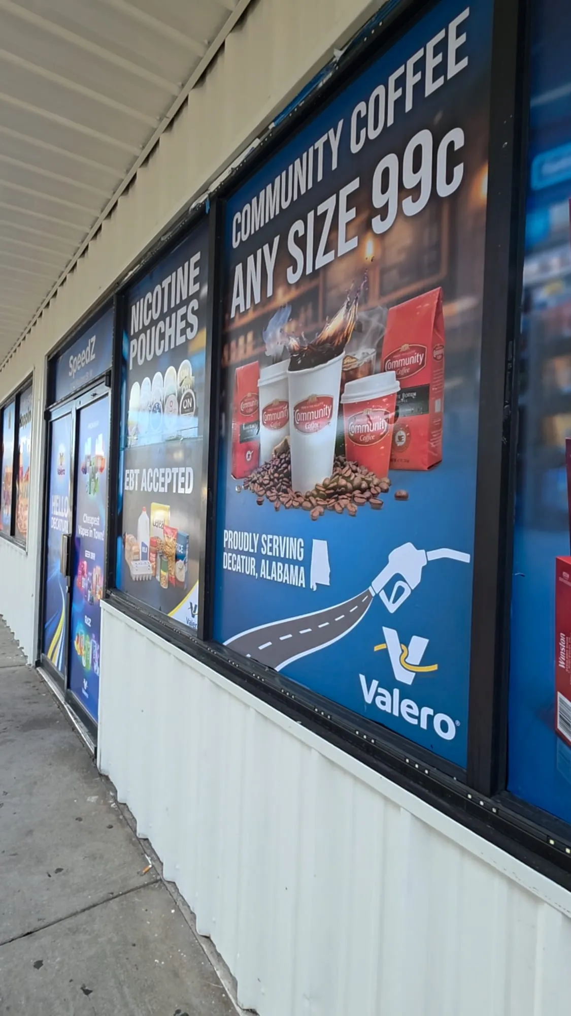 Close angled view of a large window panel with a coffee offer, steaming cups, coffee bags and a red-and-blue logo, beside narrower panels.