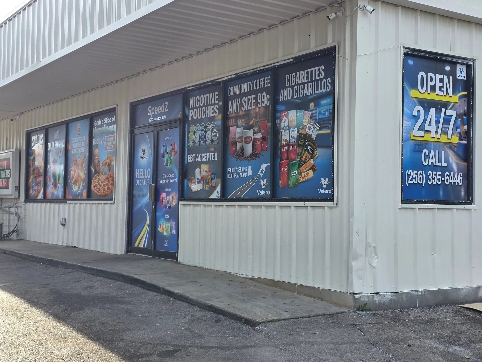 Corner of the building with every window covered in printed graphics, including a tall OPEN 24/7 panel on the right.